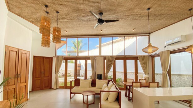 A spacious living area with a high ceiling, large windows, and a view of the outdoors. - Maravilla two bedrooms with garden view (Bali)