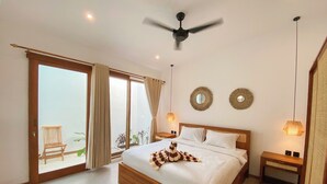 A bedroom with a wooden bed, a ceiling fan, two wall-mounted mirrors, and a view of a balcony with plants. - Maravilla two bedrooms with garden view (Bali)