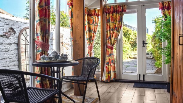 A cozy room with a wooden floor, a table with teapots, chairs, and colorful curtains. - 2 bedroom accommodation in Kings Lynn (Kings Lynn)