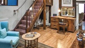 A cozy living room with a blue armchair, a wooden desk, a staircase, and a patterned rug. - 2 bedroom accommodation in Kings Lynn (Kings Lynn)