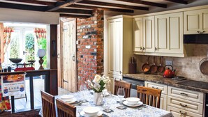 A dining area with a table set for four, a brick wall, and a kitchen with white cabinets and a red kettle. - 2 bedroom accommodation in Kings Lynn (Kings Lynn)