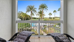 Un balcon avec deux fauteuils inclinables, une vue sur une piscine, des palmiers et, au loin, un terrain de golf.