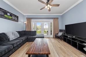 Een woonkamer met een hoekbank, een houten salontafel, een flatscreen-tv en een plafondventilator.