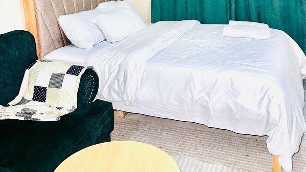 A neatly arranged hotel room with a bed, a chair, and a small round table. - La Casa Bendita (Nairobi)