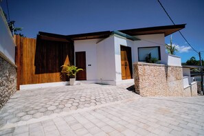A modern house with a hexagonal tile driveway, a wooden fence, and a stone wall.