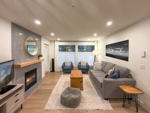 A modern living room with a fireplace, a sofa set, a coffee table, and a painting on the wall. - Stoney Creek Northstar 109 (Whistler)