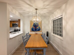 A dining room with a wooden table and chairs, a chandelier, and a bear painting on the wall. - Stoney Creek Northstar 109 (Whistler)