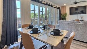 A dining area with a table set for four, a sofa, a TV, and a ceiling fan. - City Overlook w/ Pool & Extra Large Balcony (Birmingham)