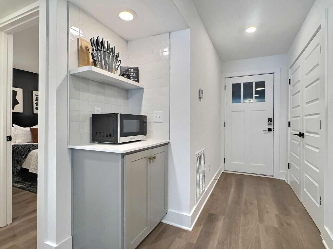 A modern kitchen with white cabinetry, a microwave, and a shelf with kitchen utensils.