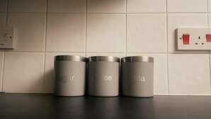 Trois récipients en acier inoxydable, étiquetés « sucre », « café » et « thé », sont posés sur un plan de travail de cuisine.