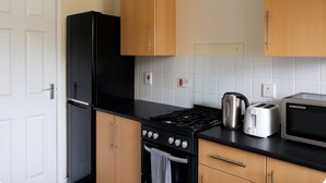 Une cuisine avec un fourneau noir, une bouilloire, un grille-pain et des armoires en bois.