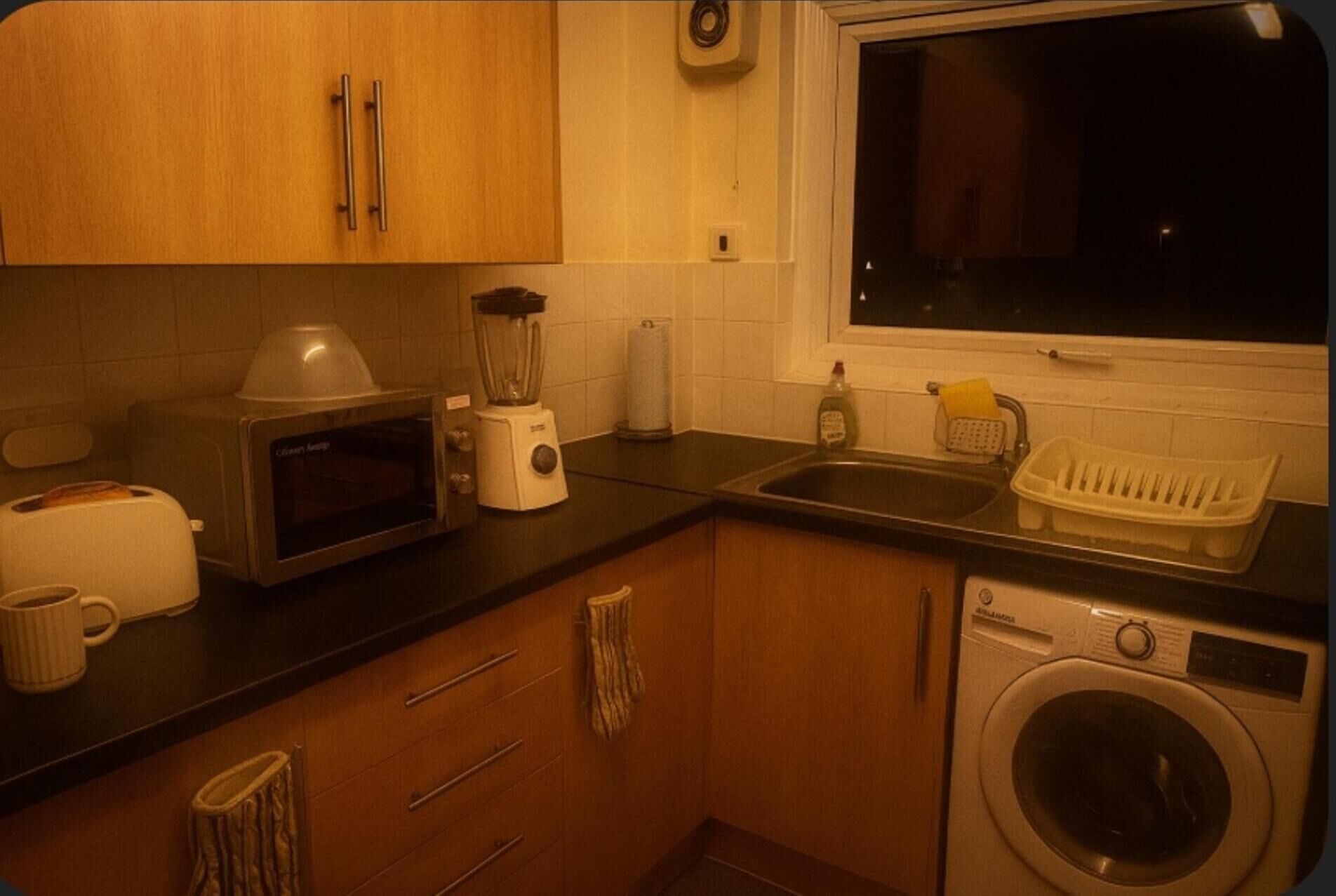 A compact kitchen with a microwave, toaster, blender, and a washing machine.