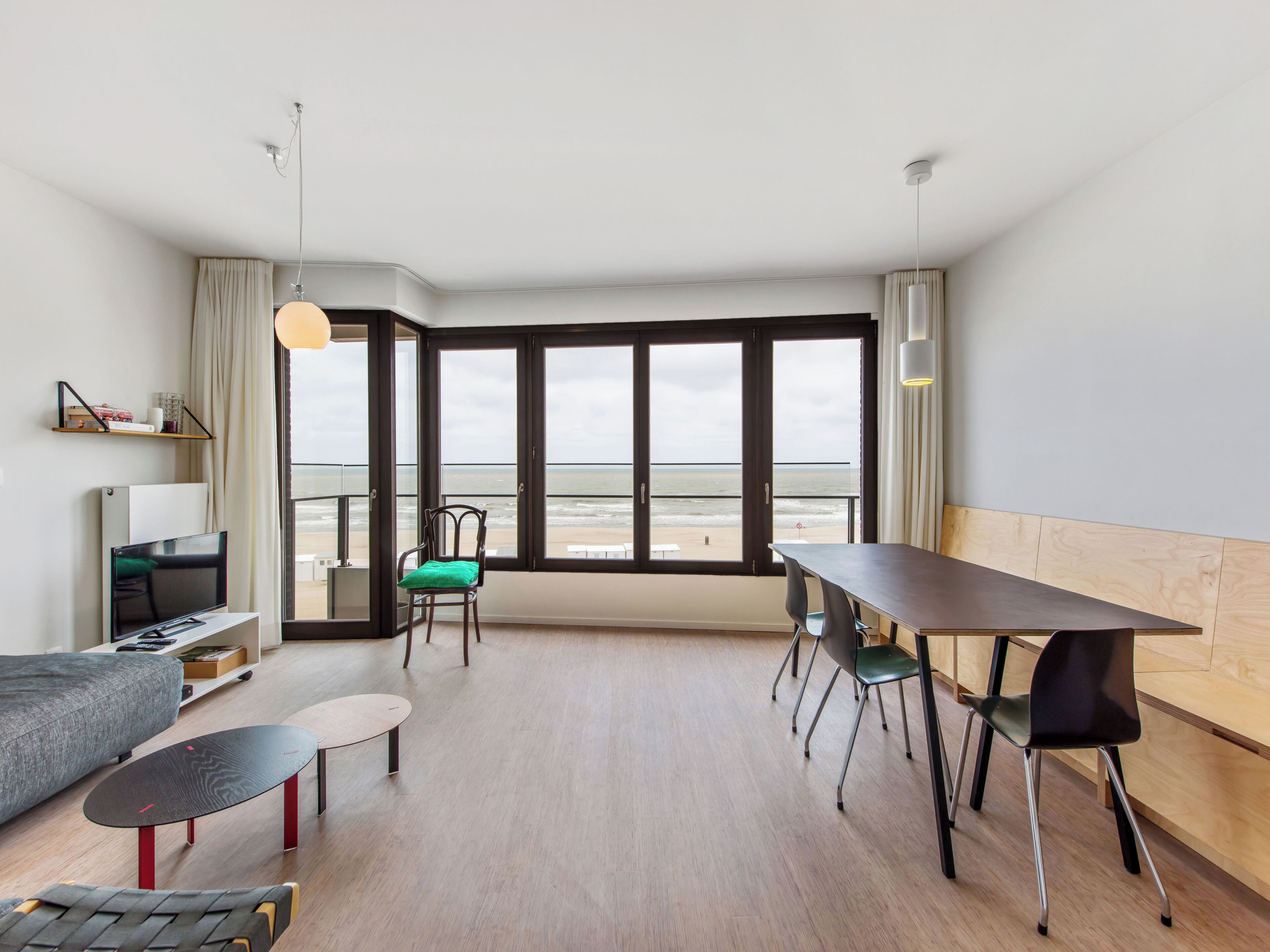 A modern room with a large window, a dining table, a sofa, and a TV.