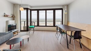 A modern room with a large window, a dining table, a sofa, and a TV.