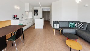 A modern, well-lit living area with a dining table, a sofa, and a coffee machine.
