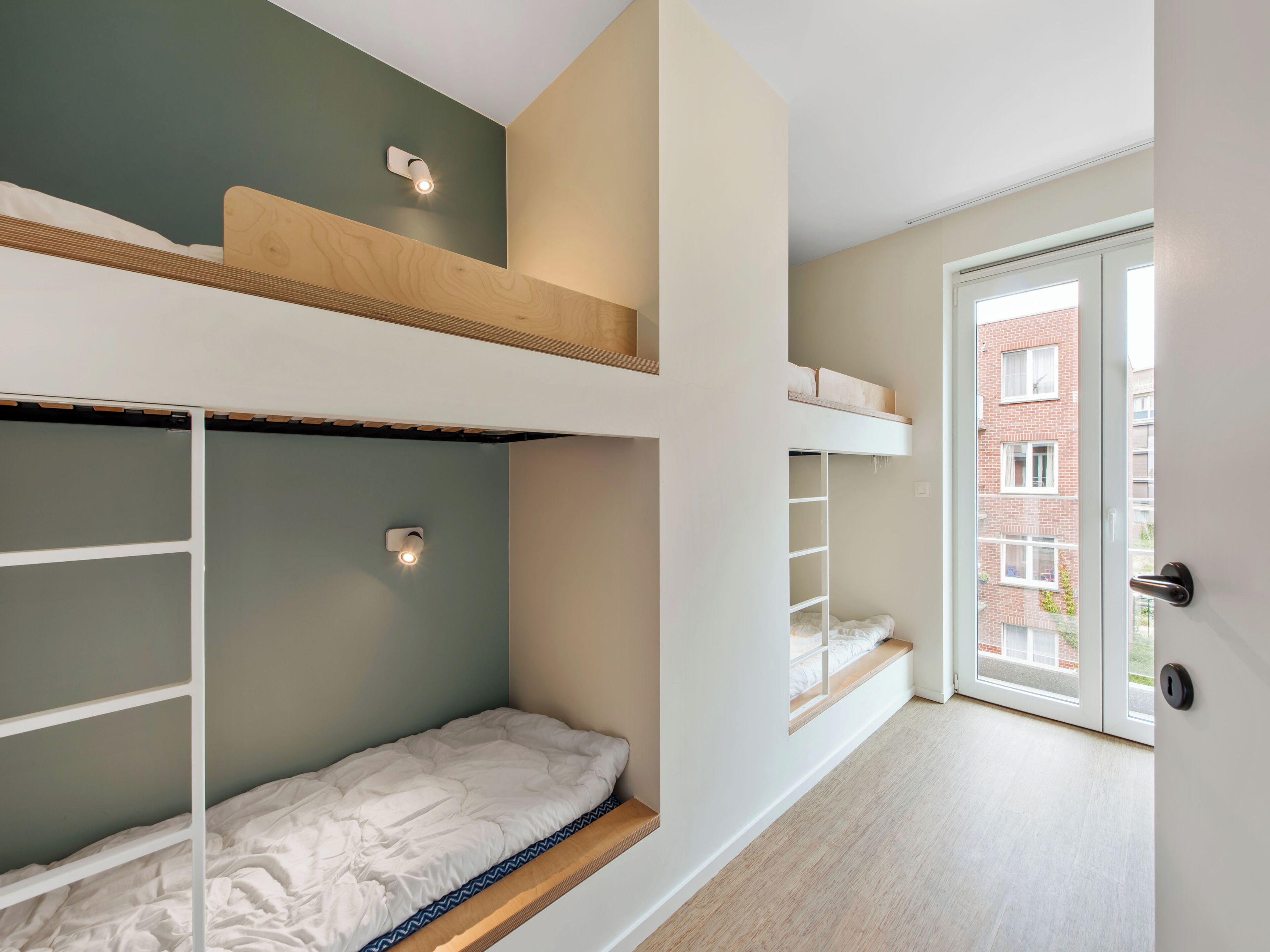 En moderne lejlighed med køjesenge, træloft og udsigt til en murstensbygning gennem en glasdør.