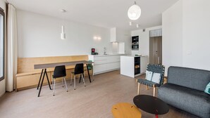 A modern, minimalist living and dining area with a wooden bench, black chairs, a grey sofa, and a small round table.