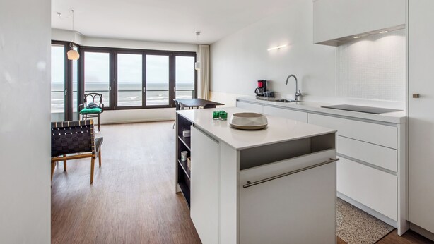 A modern kitchen with a large island, a dining area with a view of the ocean, and a seating area with a chair and table.