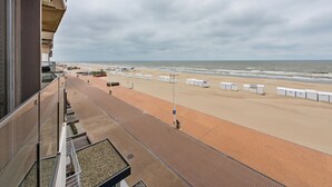 A beachside view from a balcony with a clear sky, sandy beach, and a row of white containers.