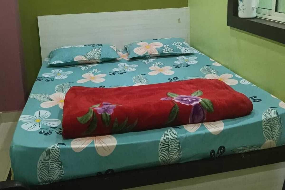 Un lit avec une literie à motifs floraux, une couverture rouge et une fenêtre avec des rideaux.