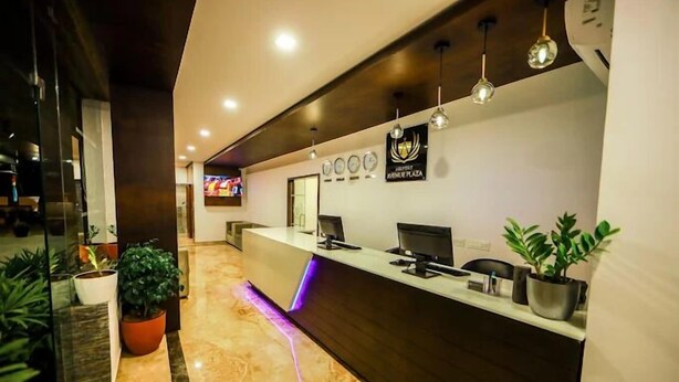 A hotel reception area with a modern design, featuring a reception desk, multiple monitors, and decorative plants. - Airport Avenue Plaza (Nedumbassery)