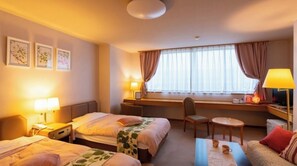 Ein Hotelzimmer mit zwei Betten, einem Schreibtisch, einem Sessel, einem Fernseher und einem Fenster mit Vorhängen.