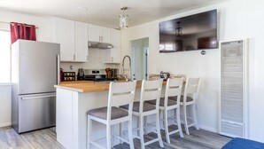 Une cuisine compacte avec des meubles blancs, un réfrigérateur en acier inoxydable, un plan de travail en bois et un îlot central intégré avec des tabourets de bar.