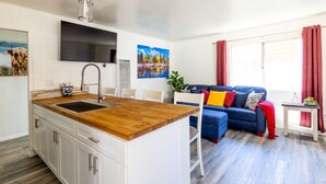Une cuisine moderne dotée d’un îlot central en bois, de meubles blancs et d’un téléviseur à écran plat fixé au-dessus de l’îlot.