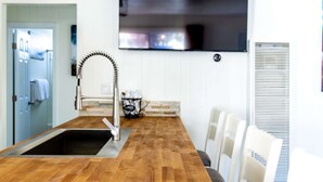 Une cuisine moderne dotée d’un plan de travail en bois, d’un évier en acier inoxydable et d’un téléviseur à écran plat fixé au-dessus du plan de travail.