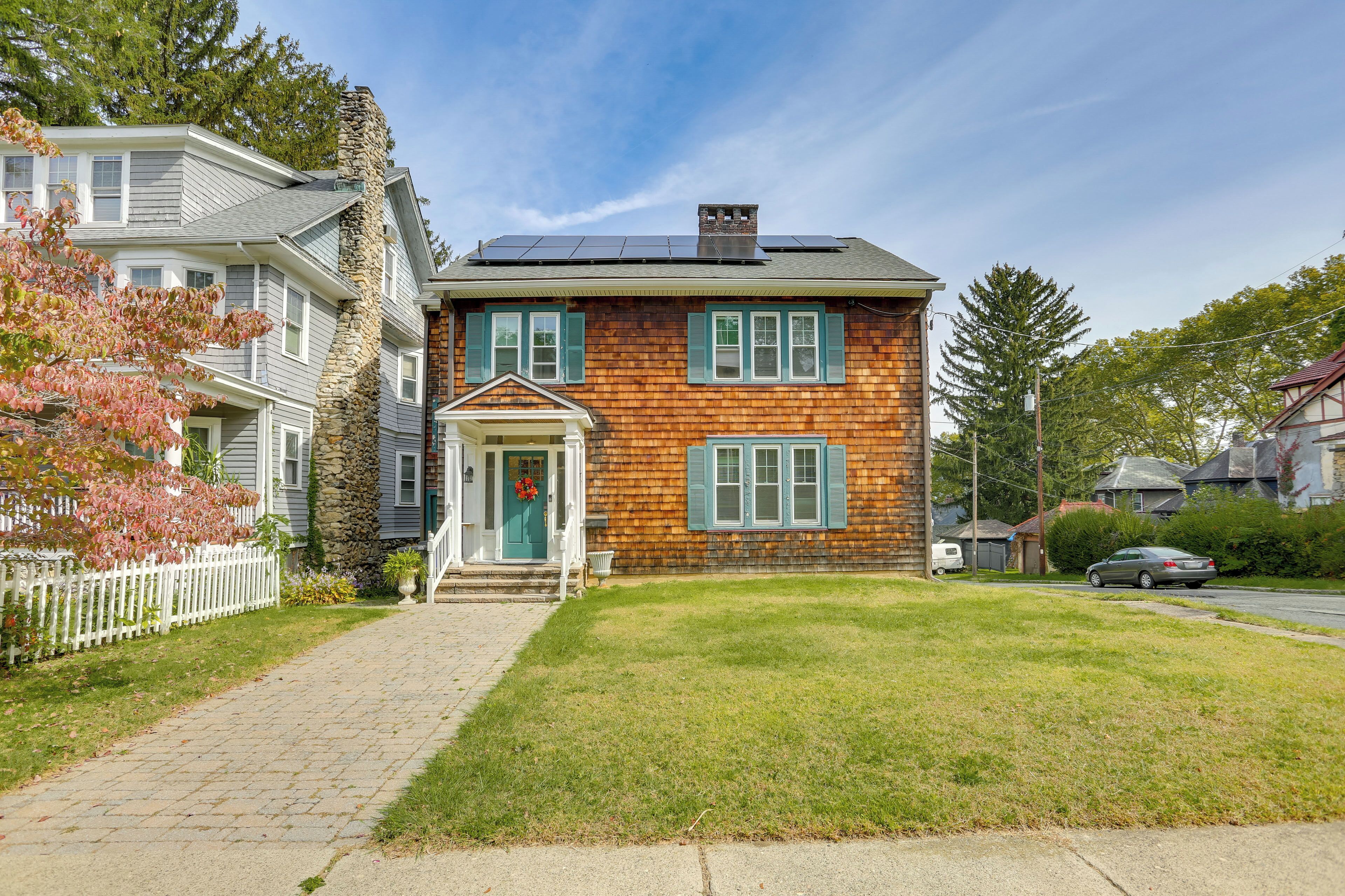 A two-story house with a stone chimney, solar panels, and a front porch.