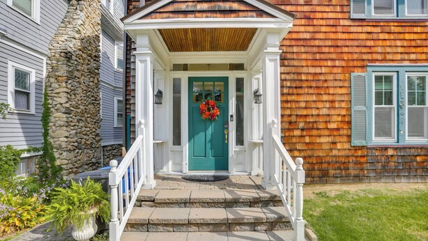 Una casa con una escalera de piedra que lleva a una puerta verde, barandillas blancas y un porche de madera.