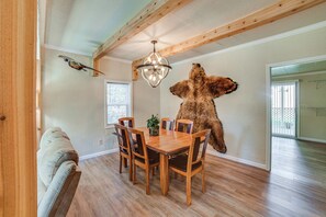Un comedor con una mesa y sillas de madera, una araña y un trozo de piel de animal montado en la pared.