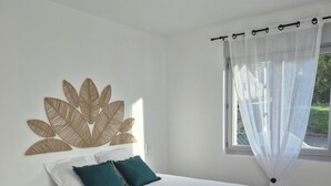 A bedroom with a large bed, a decorative wall piece, a window with sheer curtains, and a ceiling light. - Renovated house on the Route des Châteaux (Saché)