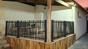 A covered outdoor area with a wooden deck and metal railing, adjacent to a white building with a balcony. - Renovated house on the Route des Châteaux (Saché)