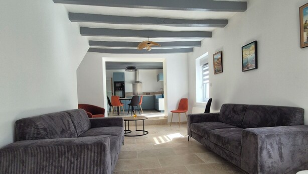 A spacious living room with two grey sofas, a dining area with a table and chairs, and a kitchen in the background. - Renovated house on the Route des Châteaux (Saché)