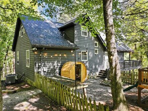 En rustik stuga med en träveranda, en bastu och en inhägnad trädgård.