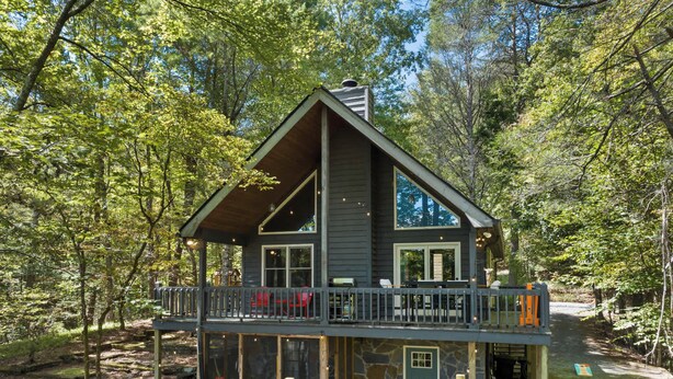 A two-story cabin with a balcony, surrounded by trees.