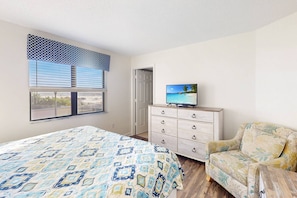 A bedroom with a bed, a dresser, a television on top, a window with blinds, and a door.
