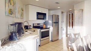 Una cocina moderna con armarios blancos, electrodomésticos de acero inoxidable, un microondas, un refrigerador y un lavamanos.