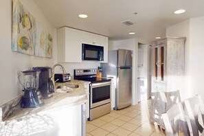 A modern kitchen with white cabinets, stainless steel appliances, a microwave, a refrigerator, and a sink.
