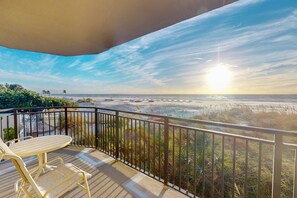 A balcony with a view of the beach and ocean during sunset.