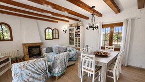 A cozy living room with a fireplace, a sofa, a dining table with chairs, and a bookshelf. - Casa Marsa - Calonge, Catalonia (Calonge)