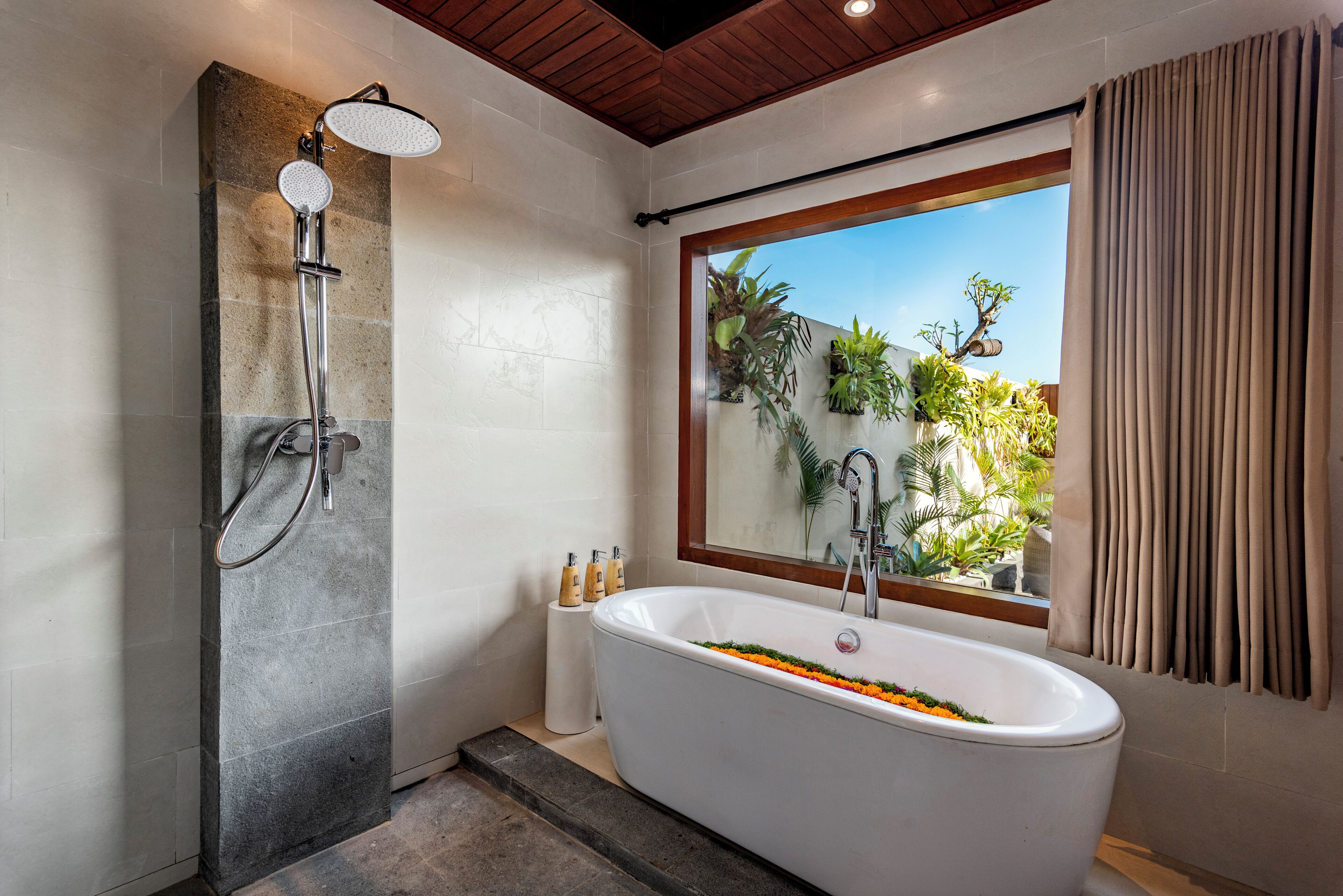 A modern bathroom with a freestanding bathtub, a shower enclosure, and a large window with a view of greenery.