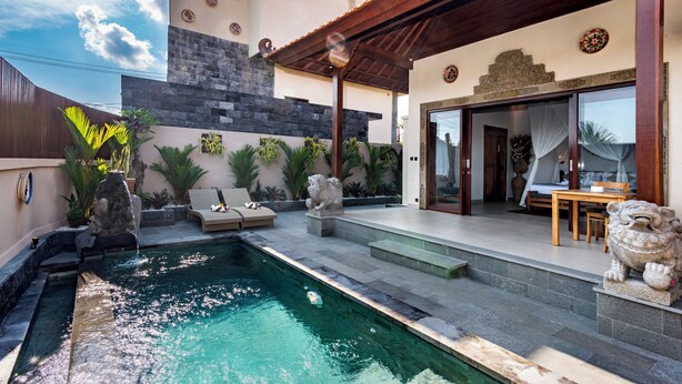 Une maison moderne dotée d’une piscine, de statues en pierre et d’un patio aménagé avec une table et des chaises.