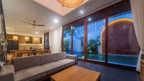 Un salon moderne avec un canapé, une table basse en bois et un coin repas, la cuisine étant visible au fond.