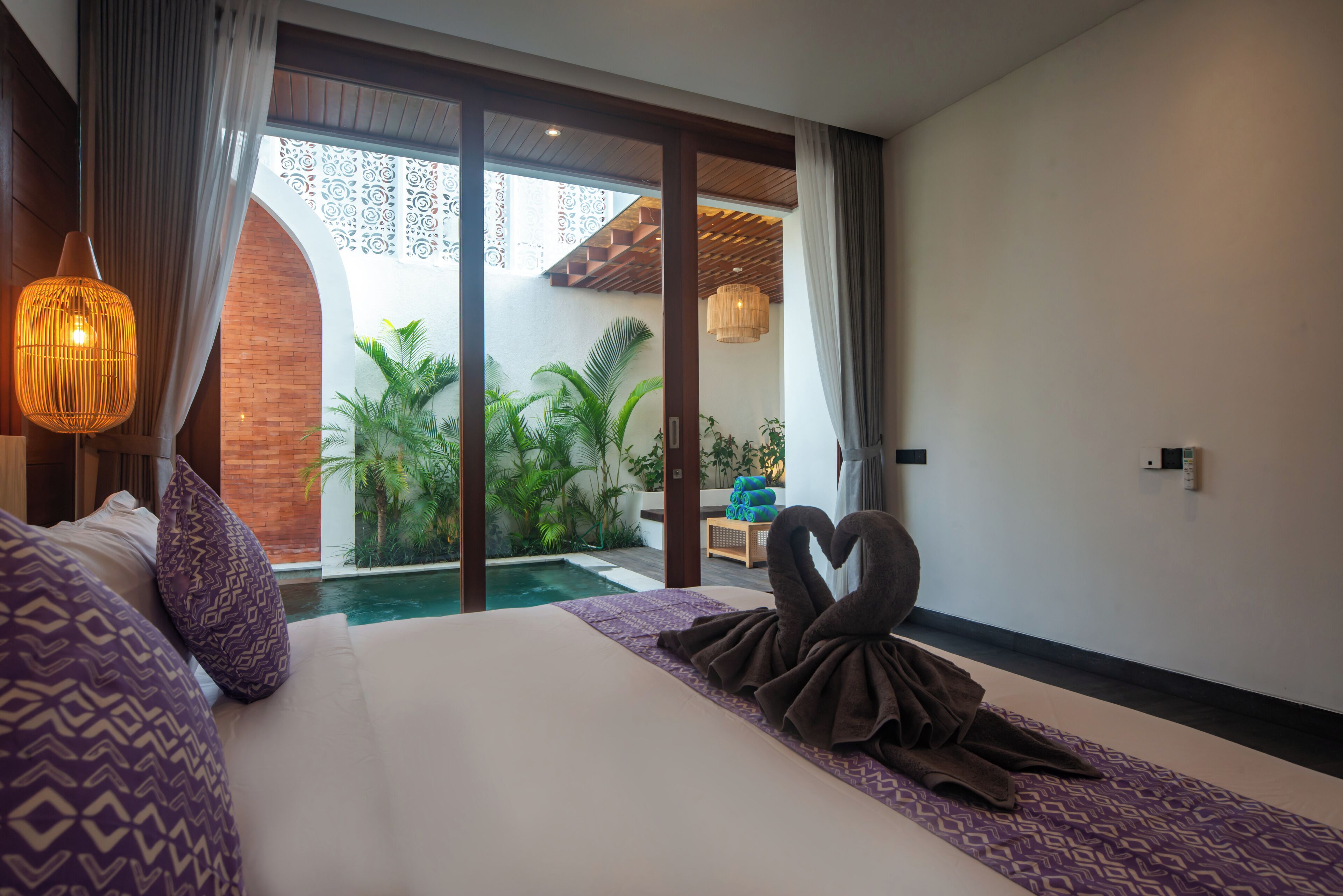 A hotel room with a large bed, a view of a swimming pool, and a balcony with plants.