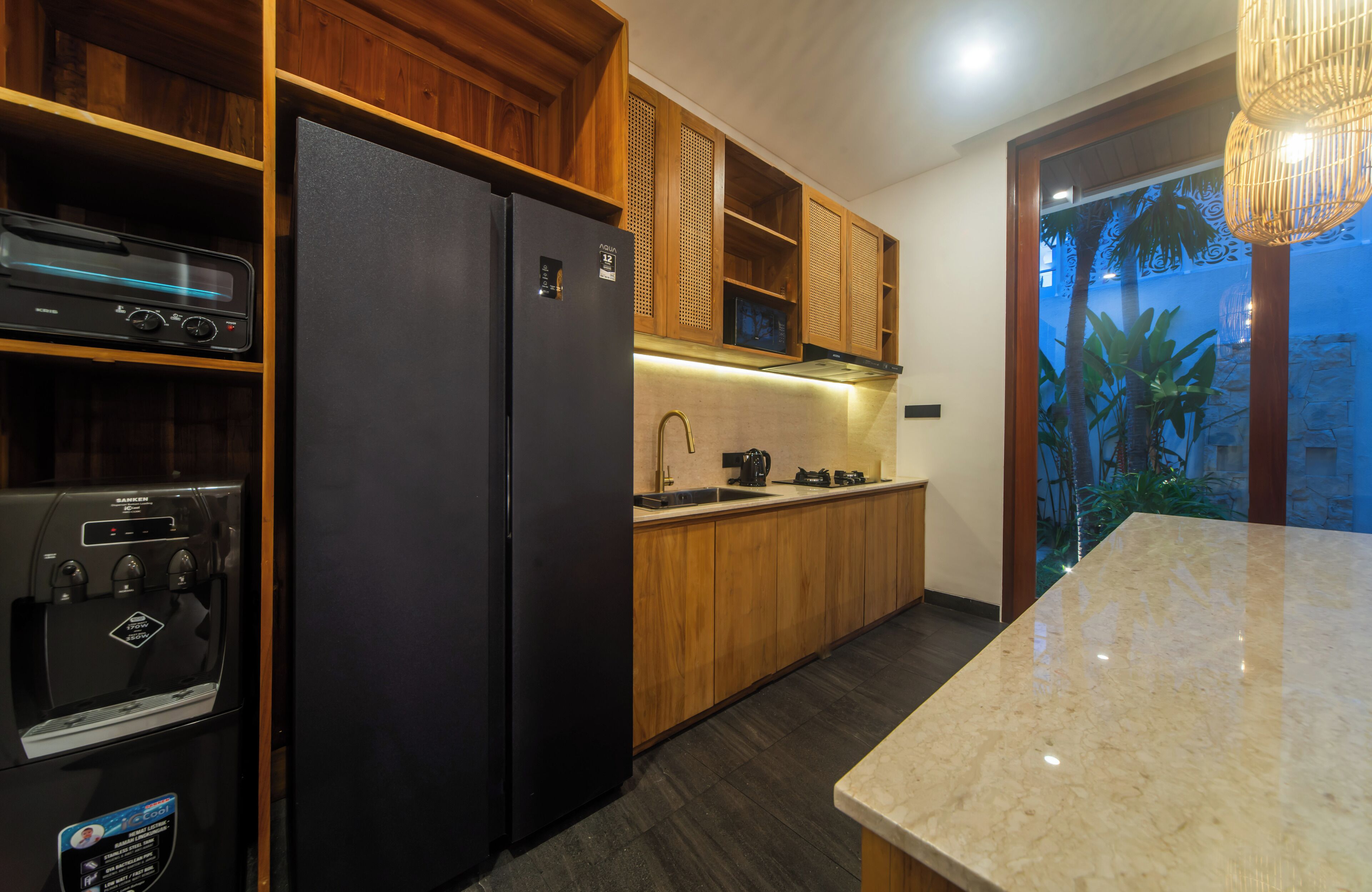 A modern kitchen with wooden cabinets, a black refrigerator, a built-in oven, and a marble countertop.