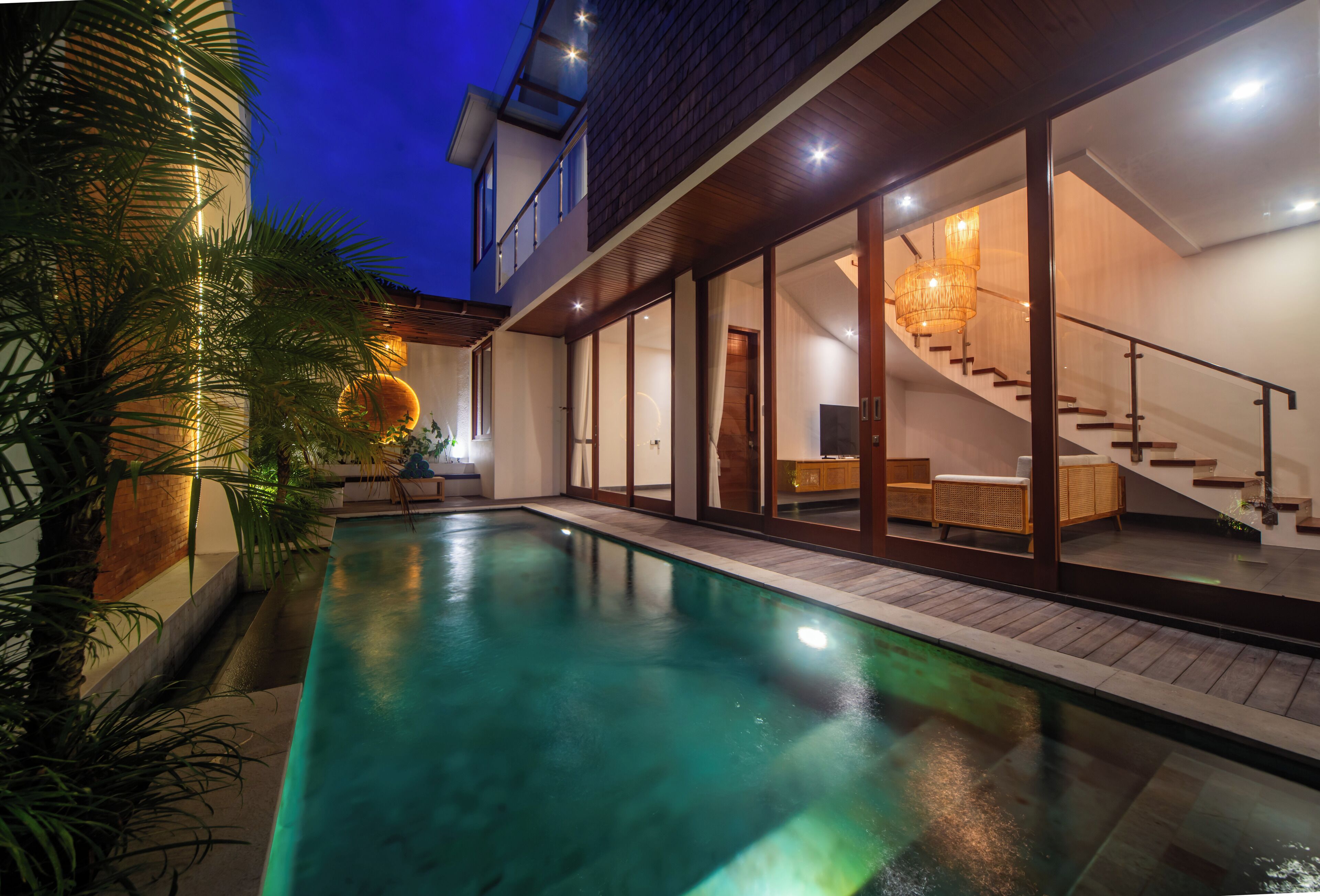A modern house with a swimming pool, a staircase, and a well-lit interior.