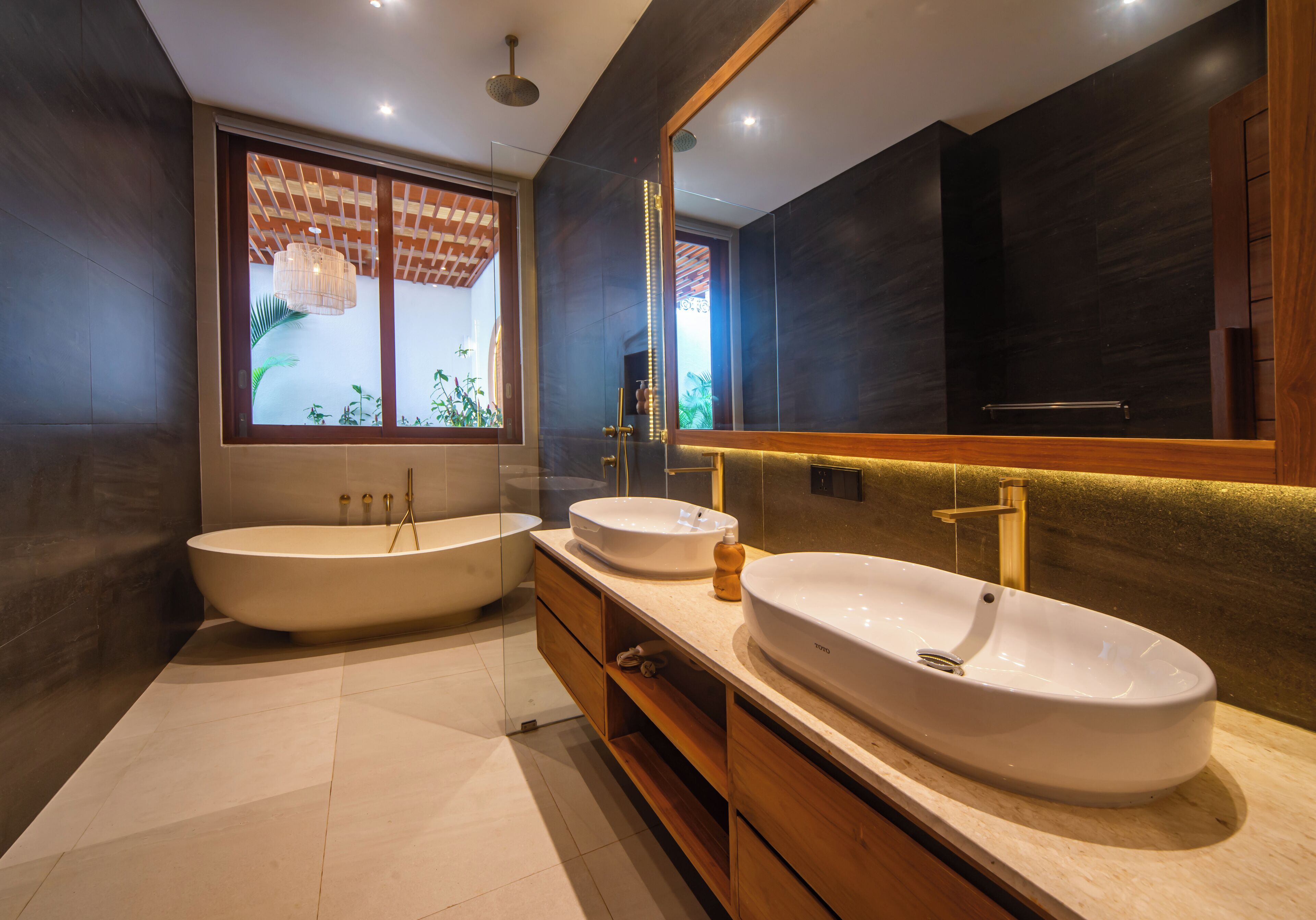 Un baño moderno con una bañera grande, dos lavamanos, armarios de madera y un espejo amplio.