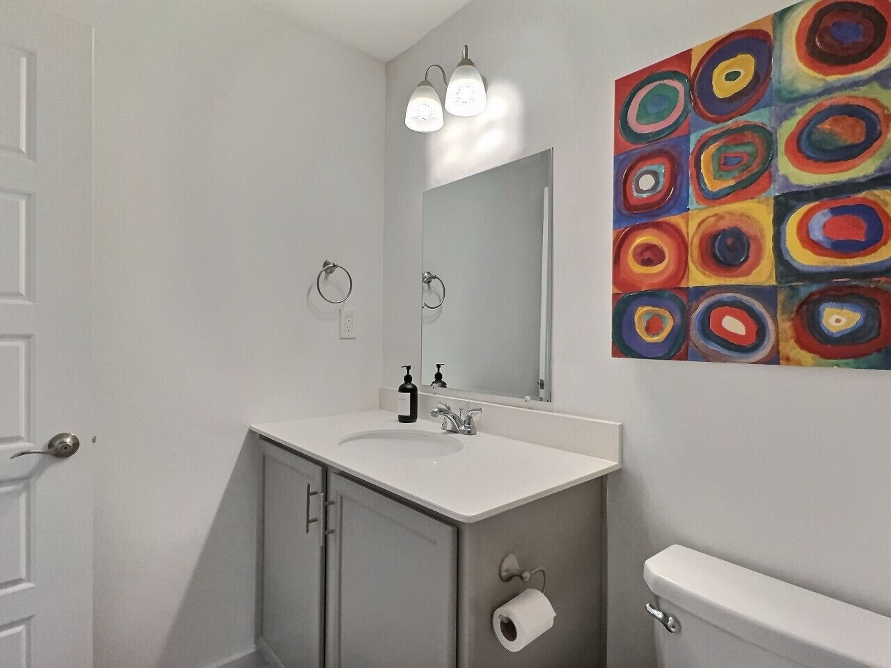 A bathroom with a white sink, a mirror, a toilet, and a roll of toilet paper.